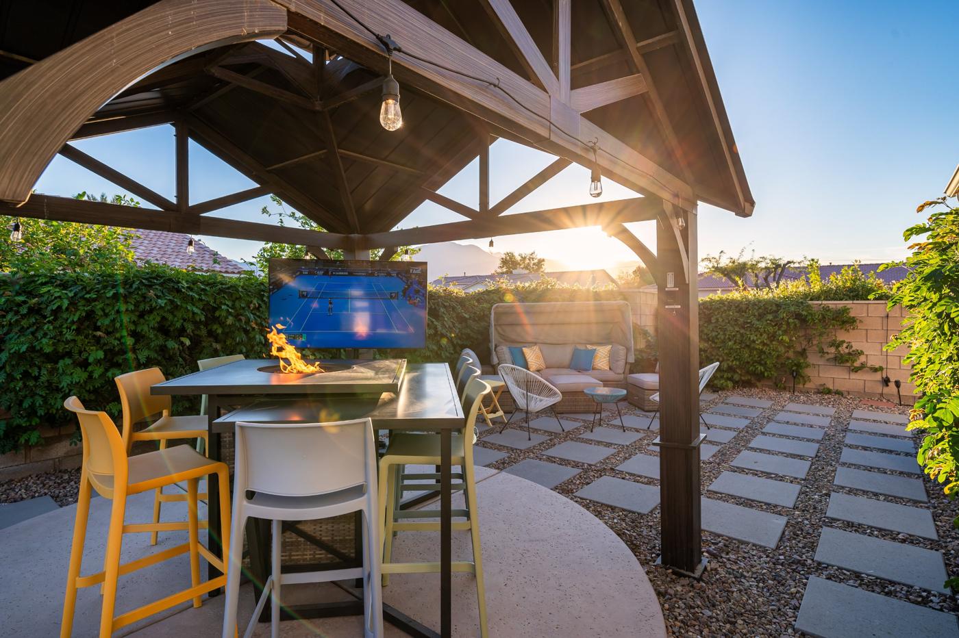 Gazebo with a fire table, bar stools and an outdoor TV at sunset