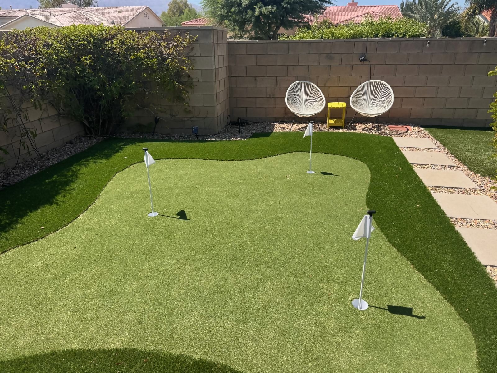Putting green in daylight with three flags, lounge chairs and a putter rack