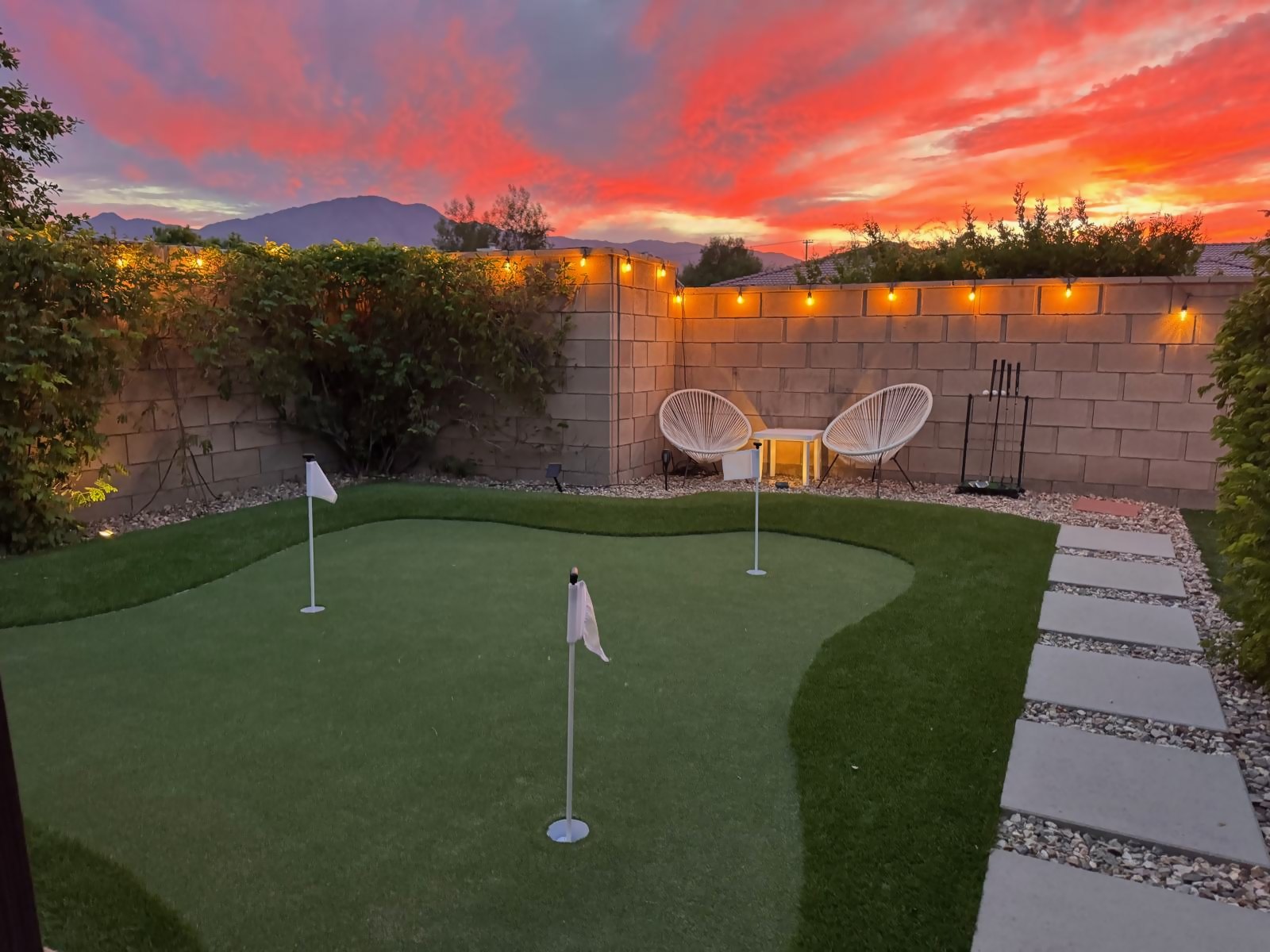 Three-hole putting green under a red and orange sunset with the Santa Rosa Mountains and string lights