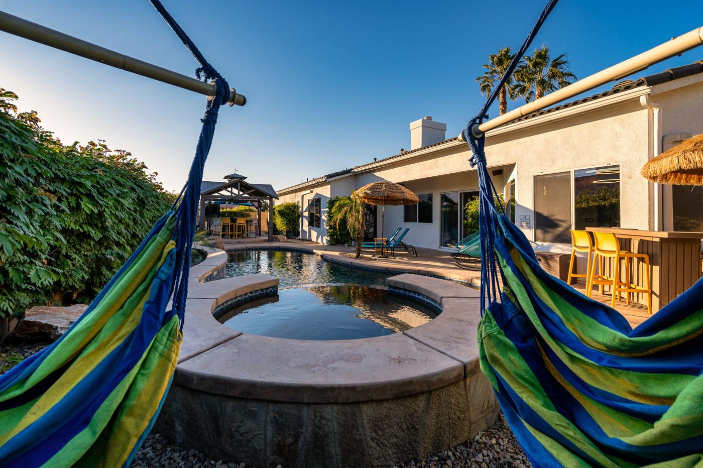 View between two hammock chairs across the spa and pool to the house