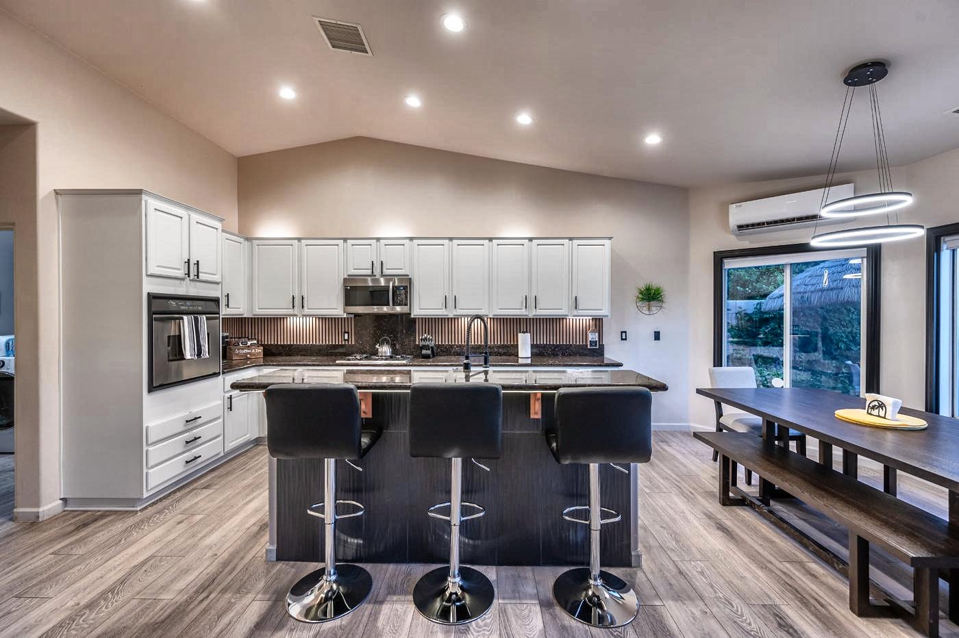 White kitchen with granite counters, island with three bar stools and a long dining table