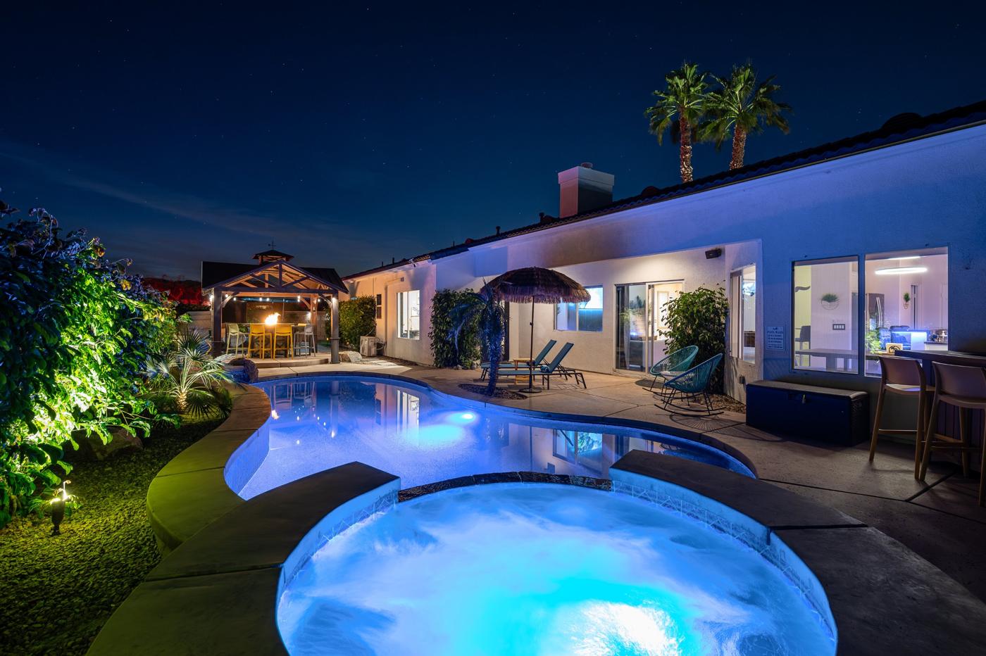 Glowing spa and pool at night with the lit gazebo fire table and palms against the stars